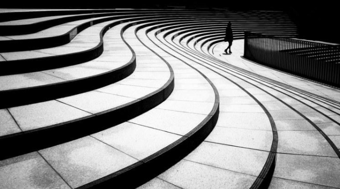 A person's silhouette walking in the distance with a series of curved steps in the foreground by Junichi Hakoyama.