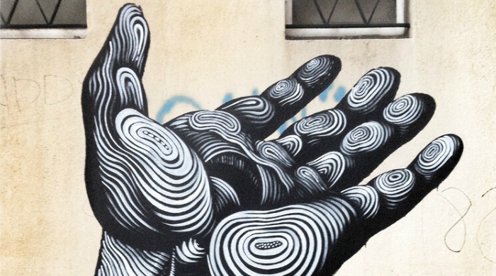 A piece of Jason Botkin's Montreal Street Art: A black hand painted on a wall with white concentric circles forming the details such as the palm and fingertips.