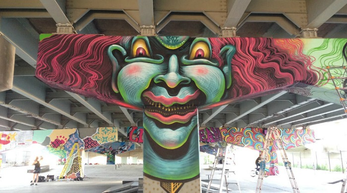 A piece of Jason Botkin's Montreal Street Art: A green face with yellow and red eyes and wild red hair painted onto a bridge support.
