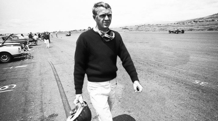 A man wearing vintage motorcycle clothing on a racetrack.