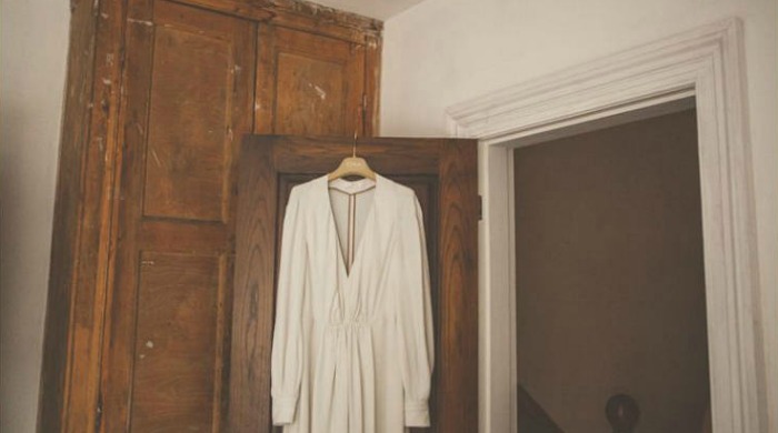 A wedding dress hanging from the back of an old wooden door.