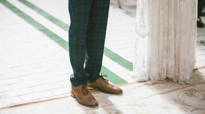 A groom wearing green tartan suit trousers and a bride in a lace dress.