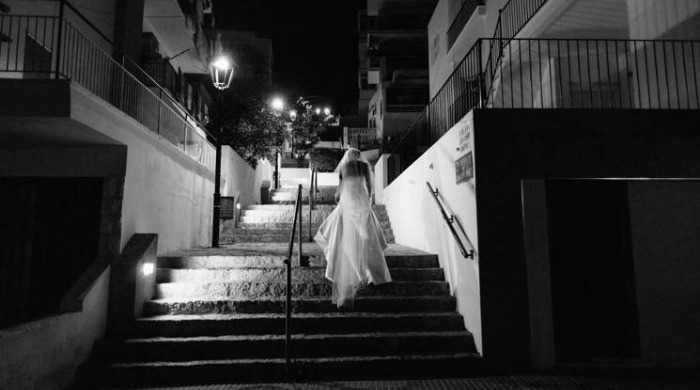 A black and white photo of a bride walking up stairs at night.