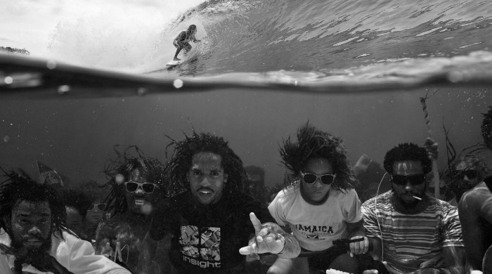 A group of Jamaicans sat under the sea with a surfer on the surface from 'Dopamine' by Dustin Humphrey.