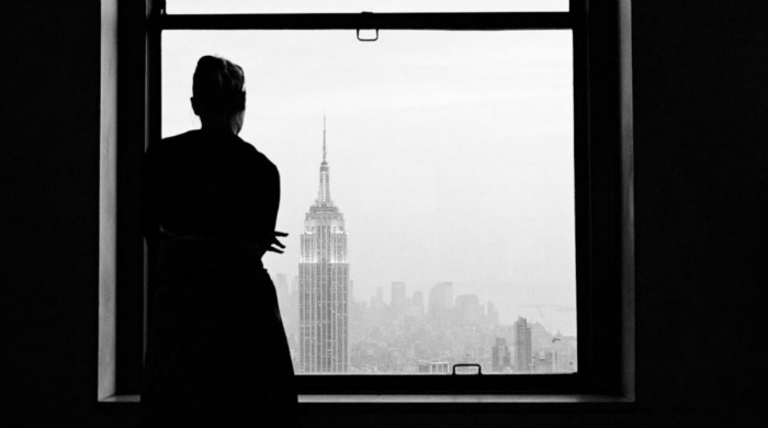 A woman looking out of a window onto the Empire State Building by Viviana Peretti.