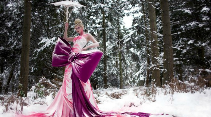 A model in a gown with a large pink bow in a snowy forest from 'Wonderland' by Kirsty Mitchell.