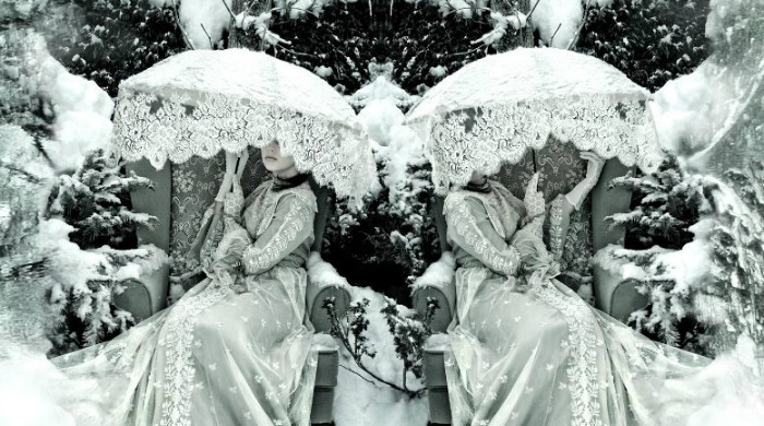 Two girls sat in chairs with white parasols in a snowy forest from 'Wonderland' by Kirsty Mitchell.