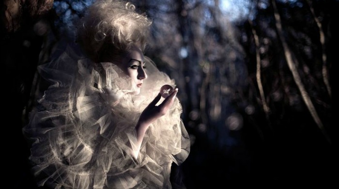 A model in a dark forest holding a small crystal ball from 'Wonderland' by Kirsty Mitchell.