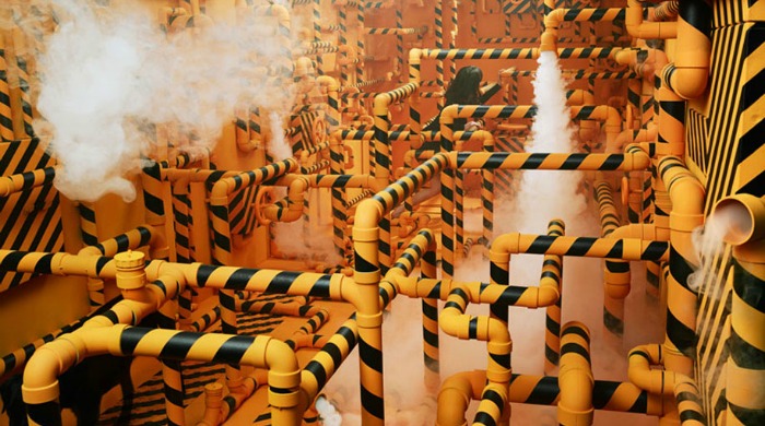 A room filled with yellow and black striped pipes with steam coming out by Jee Young Lee.
