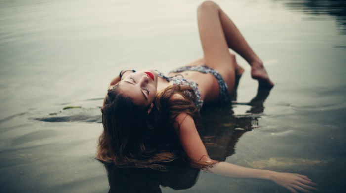 A model lying down in shallow waters in a bikini by Nirrimi Hakanson.