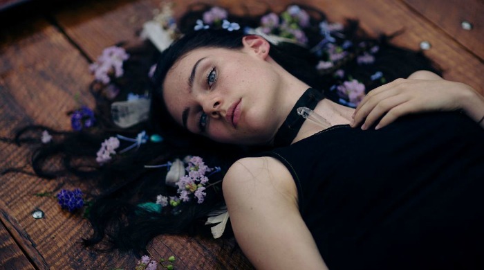 A model lying down with purple flowers in her hair by Nirrimi Hakanson.
