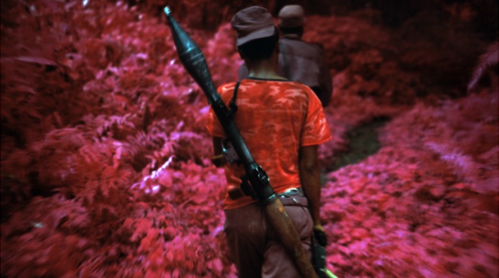 A soldier with a bazooka walking through pink foliage from 'Infra' by Richard Mosse.