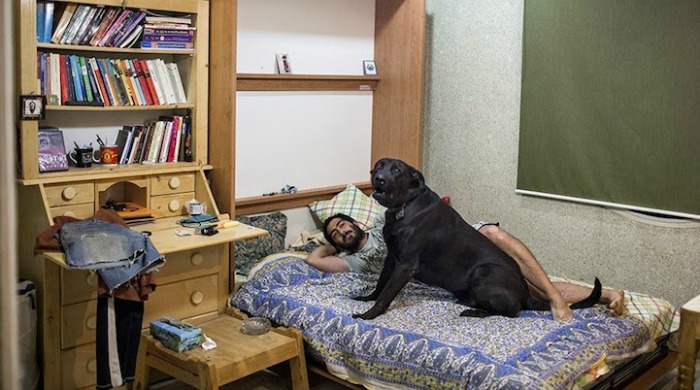 A man lying on a bed with a large black dog by Hossein Fatemi.