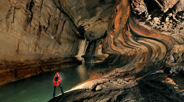 Cavers exploring a large cavern with an underground river by Robbie Shone.