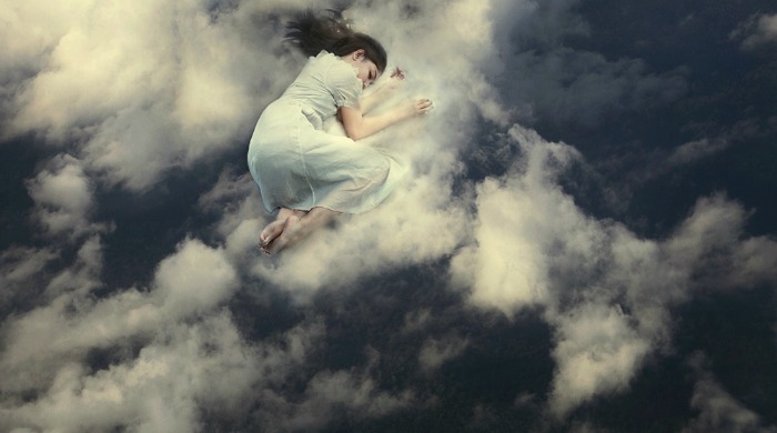 A woman curled up and sleeping on top of the clouds by Mikael Aldo.