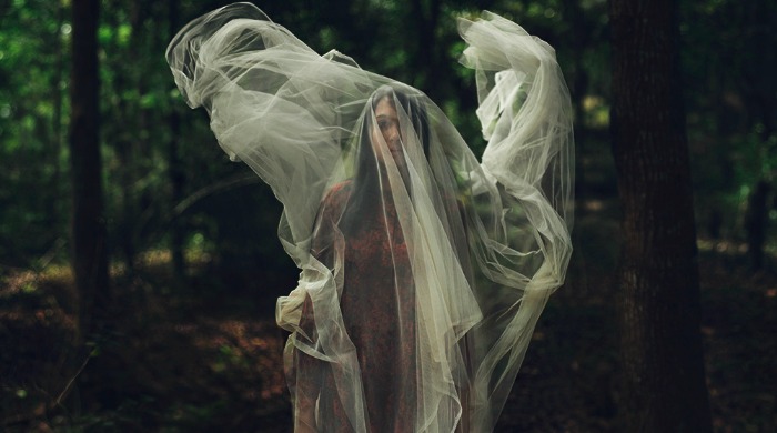 A woman in a forest covered with a floating veil by Mikael Aldo.