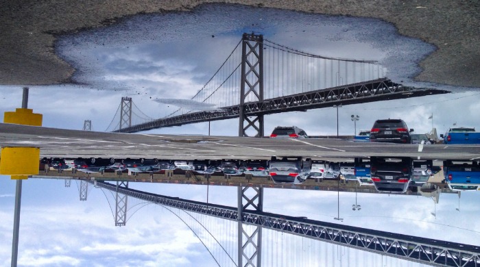 A bridge and car park reflected in a puddle by Angela May Chen.