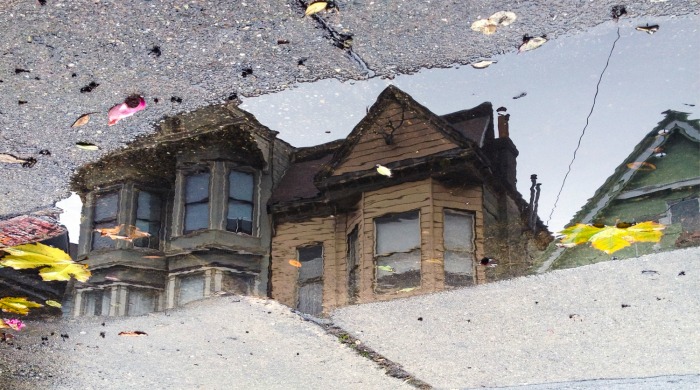 A brown house reflected in a puddle by Angela May Chen.
