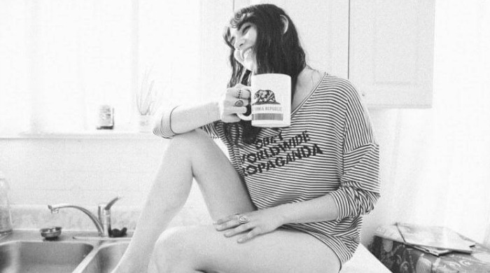 A model wearing a striped OBEY jumper holding a mug.