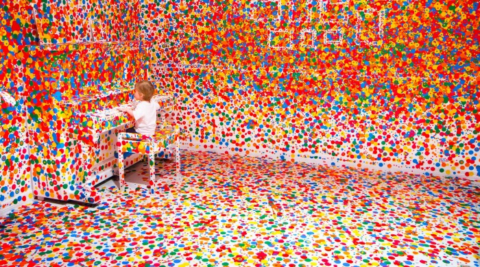 A child at a piano in the Obliteration Room, covered with colourful stickers by Yayoi Kusama.
