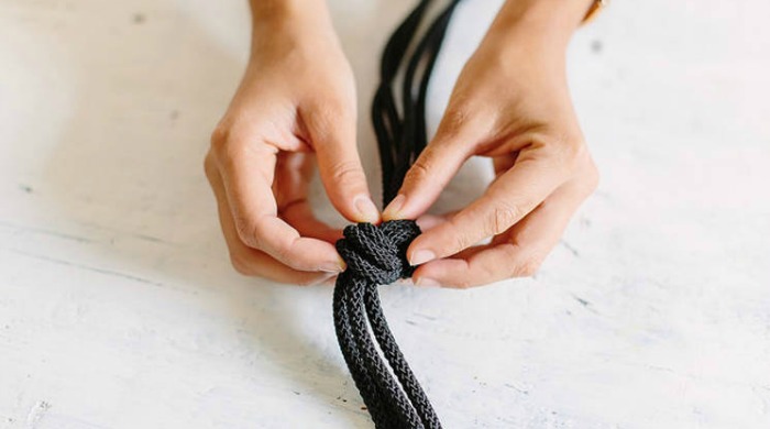 A knot being tied in black rope to create a DIY marble hanger.